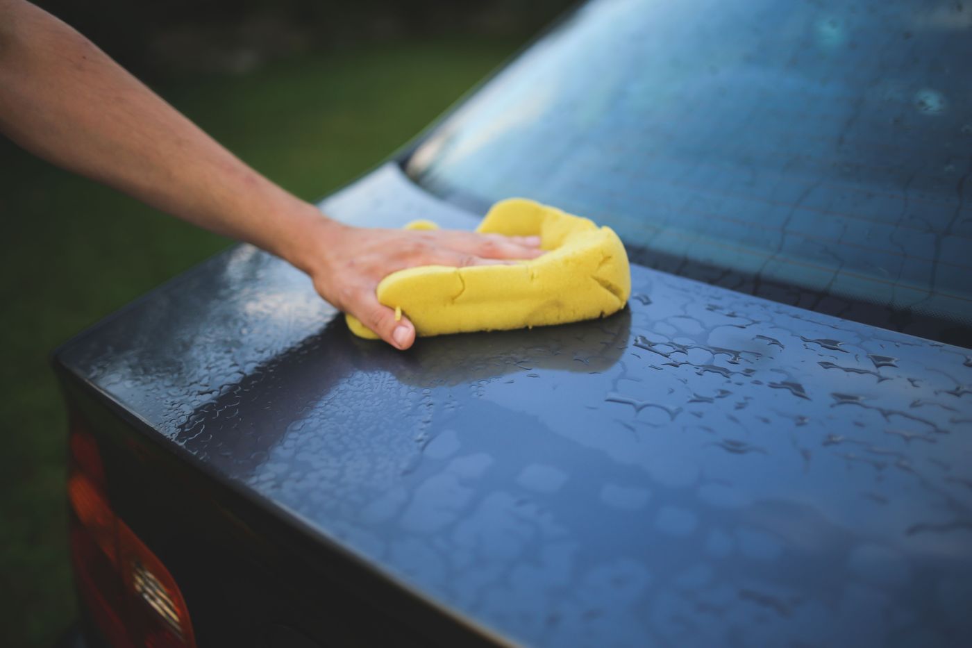 Hand polishing a glossy trunk lid with a sponge